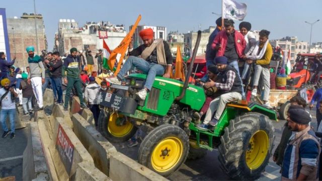 Farmers run a tractor over a barricade at the Delhi- Ghazipur border.