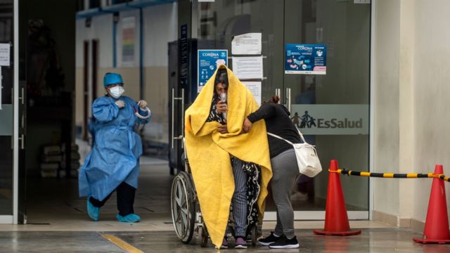 Paciente com covid em cadeira de rodas é recebido por um médico na entrada de pronto-socorro no Peru