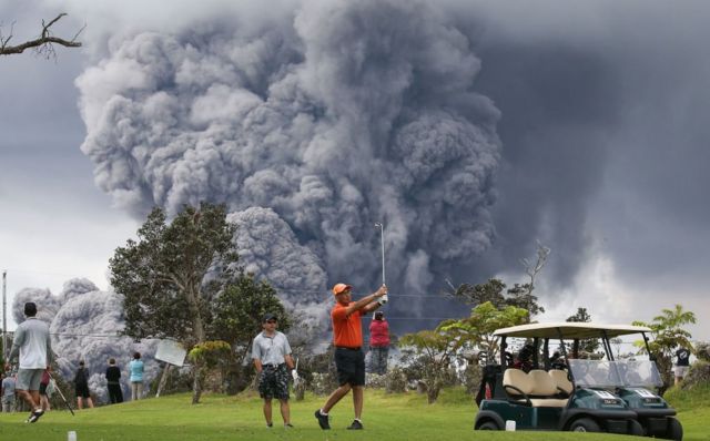 Ljudi igraju golf dok se oblak pepela uzdiše u pozadini iz vulkana na Velikom ostrvu na Havajima.
