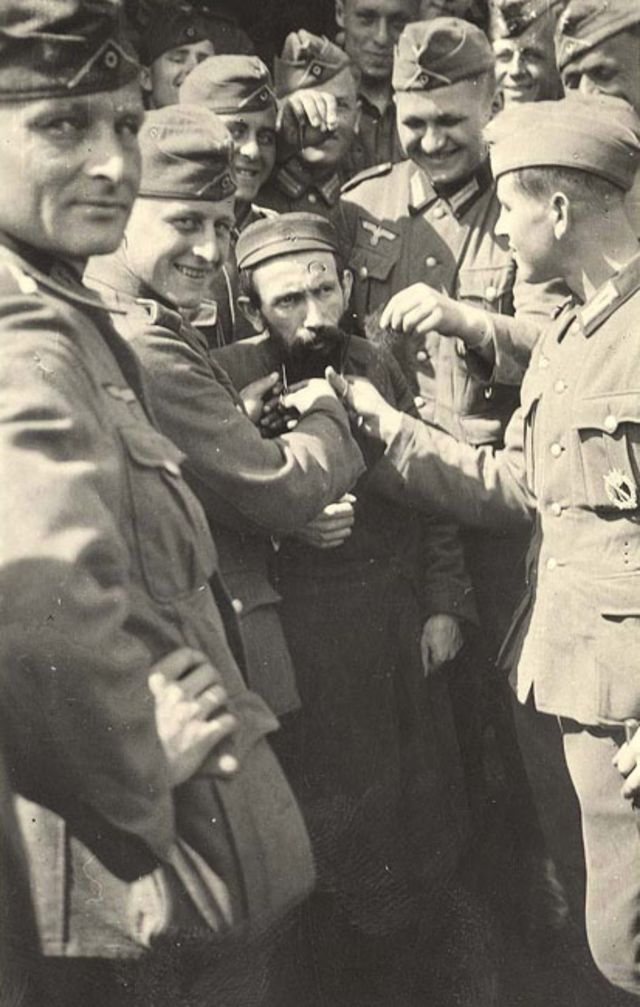 Soldados de la Wehrmacht riendo en grupo mientras le cortan la barba a un judío.
