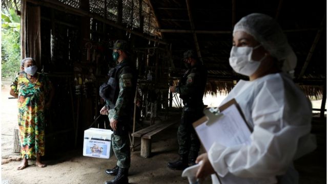 Uma trabalhadora de saúde municipal e um militar conversam com mulher indígena antes de ministrar uma vacina contra a covid nela no dia 9 de fevereiro de 2021, perto de Manaus