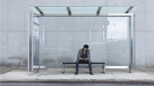 Un hombre mira su telefono solo en una estación de bus