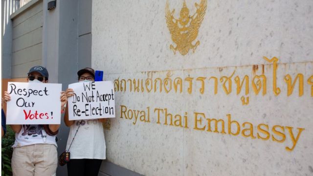 ผู้ชุมนุมชาวเมียนมาถือป้ายประท้วงที่หน้าสถานทูตไทยในย่างกุ้ง 24 ก.พ. 2564