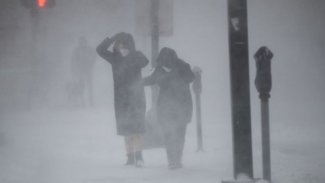 Dos personas caminan y se protegen del viento entre la nieve.