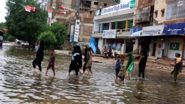 نساء وأطفال يعبرون شارعا غمرته المياه في كراتشي
