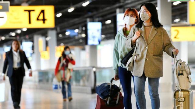 Three travellers at Amsterdam's Schiphol Airport wearing masks