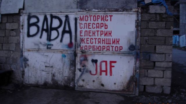Надпись красной краской на белых, железных дверях: "моторист", "слесарь" "Електрик", "жестянщик", "карбюратор"