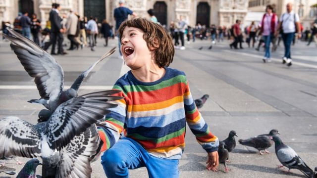 Um menino jogando alguns pombos em uma praça