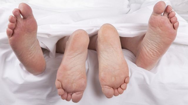Pés de duas pessoas sob os lençóis de uma cama