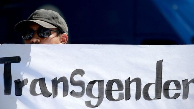 Un manifestante sostiene una pancarta que dice "transgénero".
