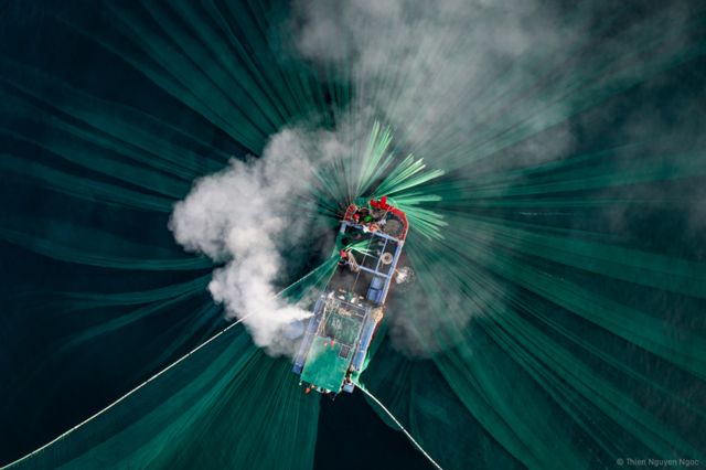 Una fotografía aérea de humo saliendo de un bote, con redes verdes en el agua.