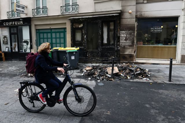 A cyclist rides her bicycle past a burnt store and damage in a street the day after clashes during protests over French government's pension reform in Paris, France, March 24, 2023.