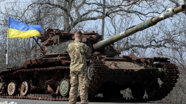 جندي يقف أمام دبابة ترفع علم أوكرانيا