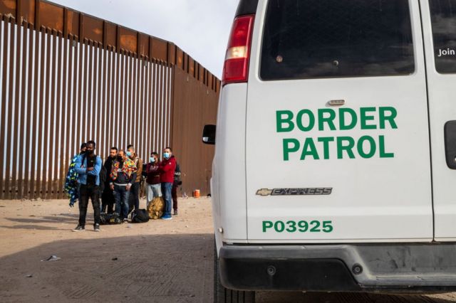 Migrantes tomados en custodia por la Patrulla Fronteriza en Yuma, Arizona, junto al muro que separa Estados Unidos de México, el 7 de diciembre de 2021.
