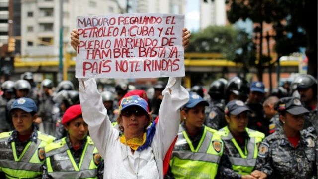 A woman holds a sign that reads: "Maduro gives oil to Cuba and people die of hunger. Enough. Country do not give up" during a protest of workers of the health sector due to the shortages of medicines and for higher wages, outside a public children hospital in Caracas, Venezuela August 16, 2018.