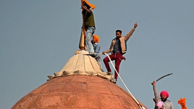 Manifestantes sobem em uma cúpula nas muralhas do Forte Vermelho em Delhi