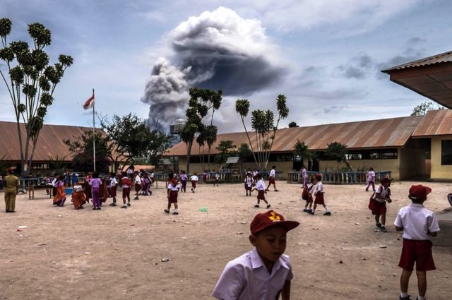 Student play outside their classrooms while Mount Sinabung spews volcanic ash