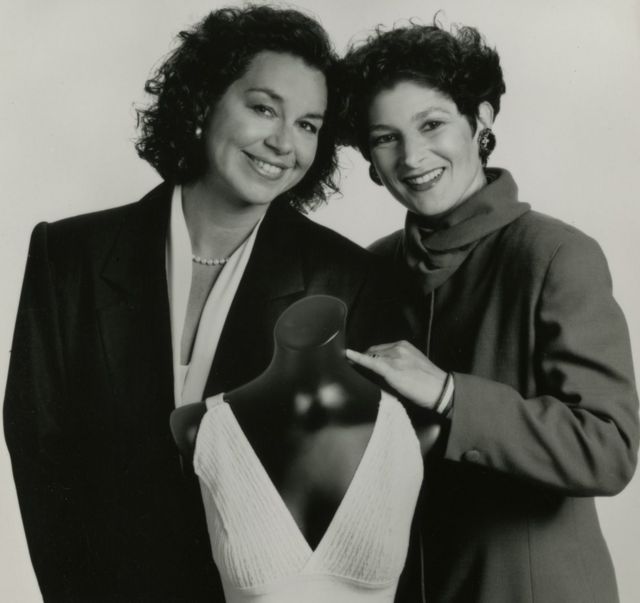 Fotos em preto e branco mostra Lisa Lindahl e Hinda Miller, duas mulheres brancas de cabelo preto encaracolado, ao lado de um manequim com uma peça de roupa antiga
