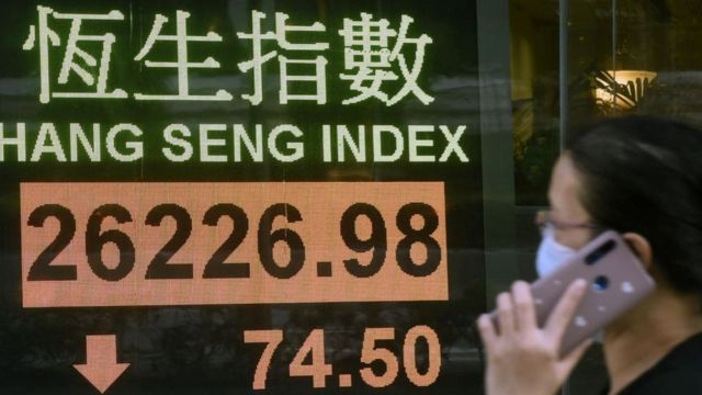 A woman passes through a screen showing the development of a Chinese stock index.
