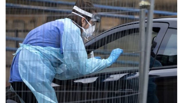Profissional de saúde usa um cotonete para coleta de amostras pela janela do carro em um 'drive-thru' de exames em Edimburgo