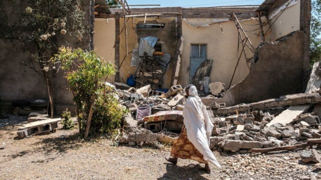 A woman walks in front of a damaged house which was shelled as federal-aligned forces entered the city, in Wukro, north of Mekele, on March 1, 2021
