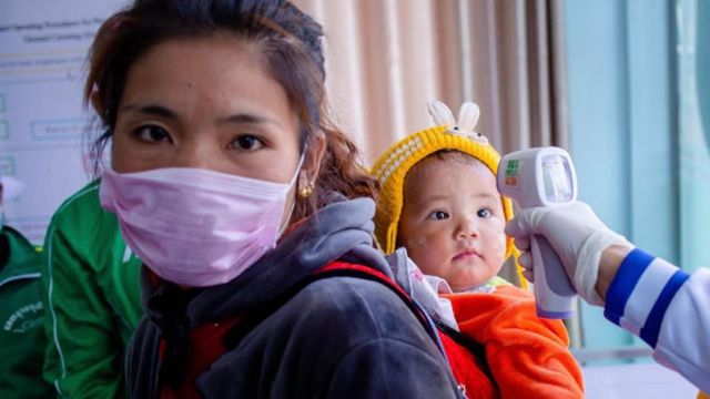 Nhân viên y tế kiểm tra nhiệt độ của một em nhỏ tại biên giới Myanmar và Trung Quốc