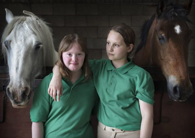 Portrait of sisters Hattie & Charlotte stood with horses from the on-going project, Our Human Condition, by Paul Wenham-Clarke in 2017.