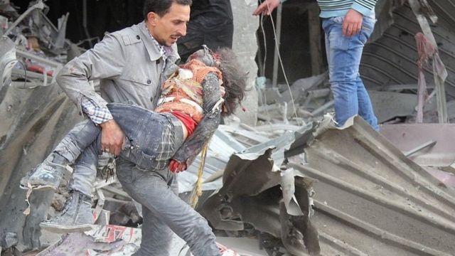 صورة من الأرشيف: رجل سوري يحمل طفلة مصابة في غارات جوية لقوات النظام السوري على سوق في حي تسيطر عليه المعارضة في إدلب، سوريا في 2 فبراير / شباط 2014.