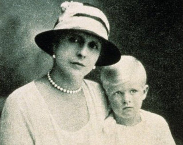 Princess Alice holds her toddler Prince Philip on her lap in a black and white portrait picture
