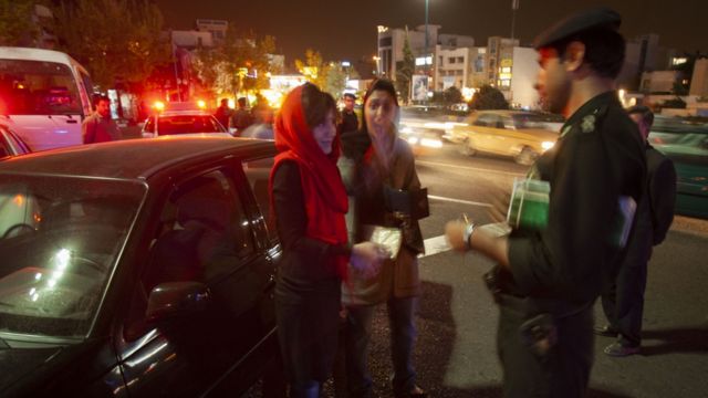 Seorang petugas polisi moral berbicara dengan dua wanita.