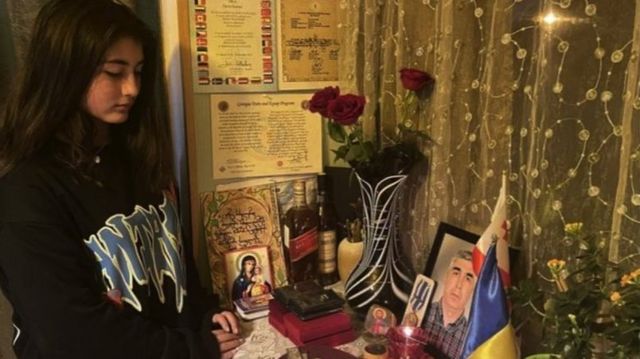 David Ratiani's daughter, Mariam, looks at a picture of her father on a desk surrounded by Ukrainian and Georgian flags and roses.