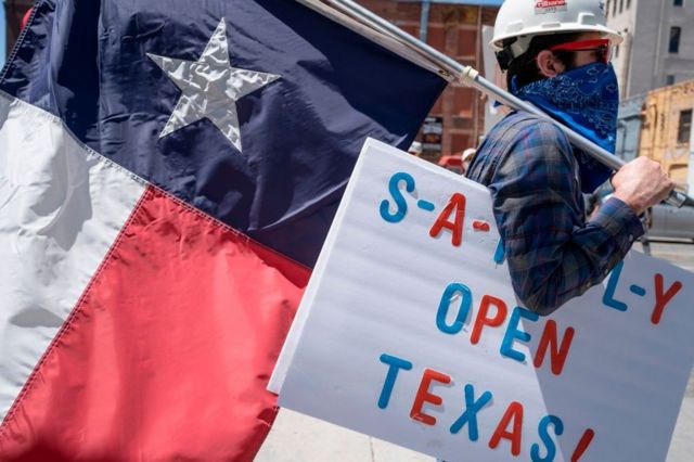 Un hombre lleva una bandera de Texas y un cartel que pide que abran el estado.