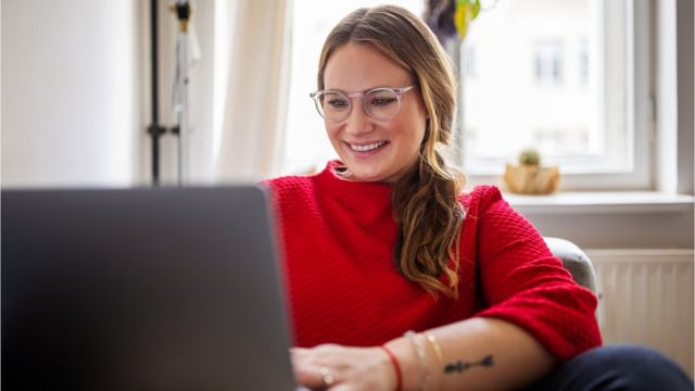 Mulher branca com blusa vermelha trabalha em frente a computador