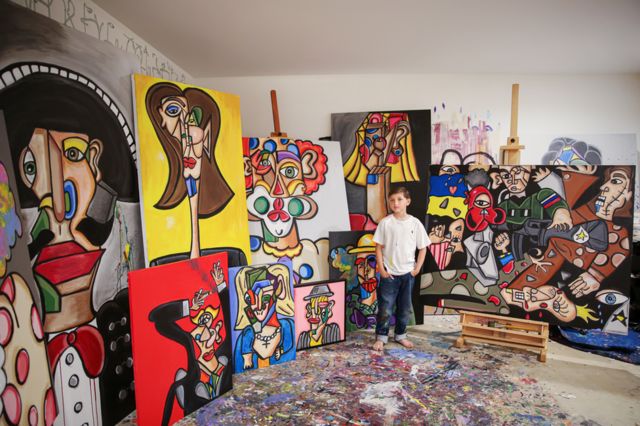 Andrés Valencia em seu ateliê, cercado por suas pinturas