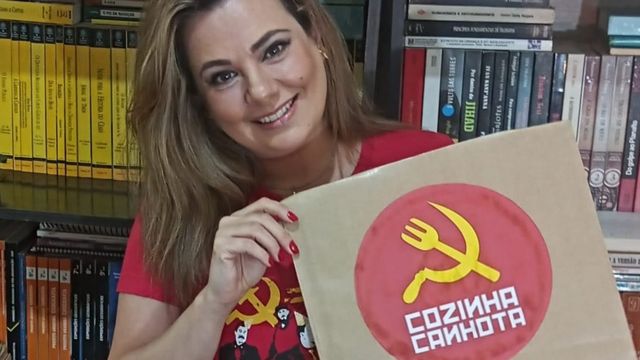 Marcelle Nogueira Toscani segura embalagem de papel com o logotipo de sua marmitaria vegana Cozinha Canhota, que contém a imagem de um garfo e foice, com o garfo no lugar do martelo do símbolo do comunismo