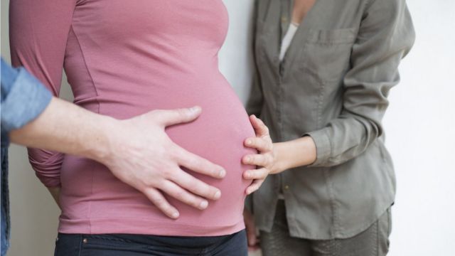 Un hombre y una mujer ponen sus manos sobre el vientre de una embarazada.