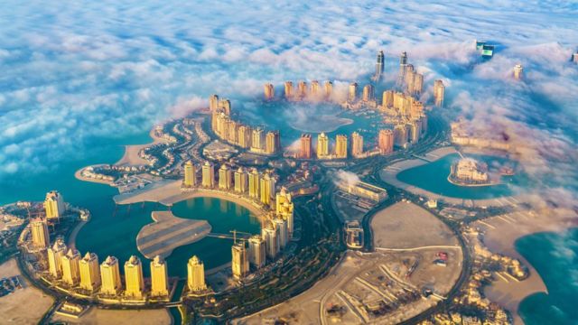 Fotografia colorida mostra vista aérea de uma ilha com três baías e muitos prédios altos