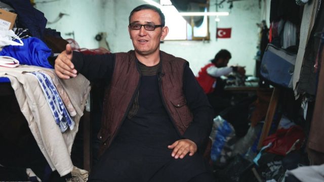 Islam Qaracha sits in a room surrounded by textiles