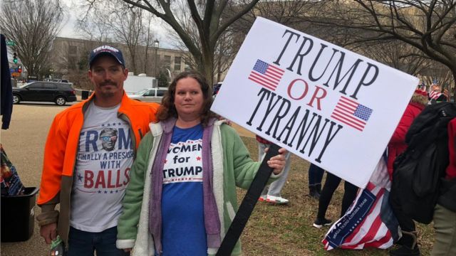 Joe Shields ao lado de mulher, que segura placa dizendo em inglês: 'Trump ou tirania'