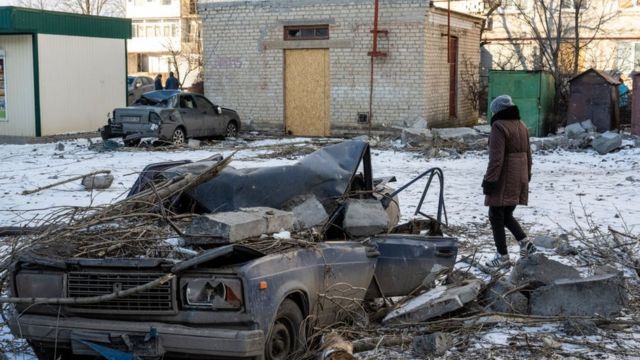 Una mujer camina junto a un coche destrozado por la caída de hormigón de concreto, luego que explotara un misil ruso.