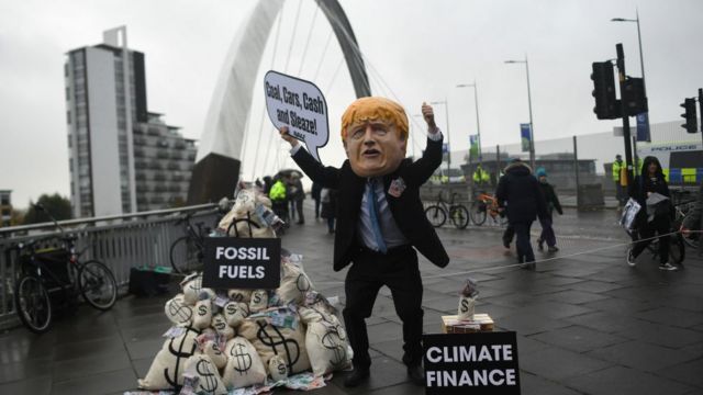 Un manifestante con una máscara del primer ministro Boris Johnson sostiene un cartel que dice "¡Carbón, coches, dinero y sordidez!".