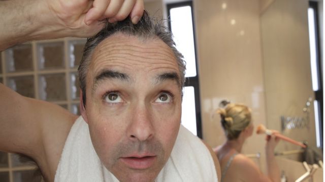 Hombre se toma el cabello con sorpresa mientras está en el baño.