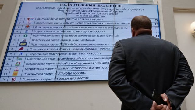 Мужчина изучает изображение предвыборного бюллетеня для выборов в Госдуму-2016 на плазменном экране