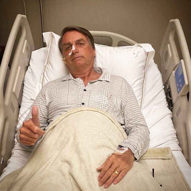 Bolsonaro faz aceno de positivo com a mão deitado em cama de hospital