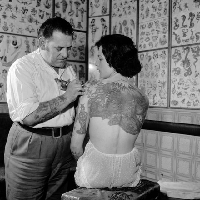 Tatuador tatuando hombro de Pam Nash