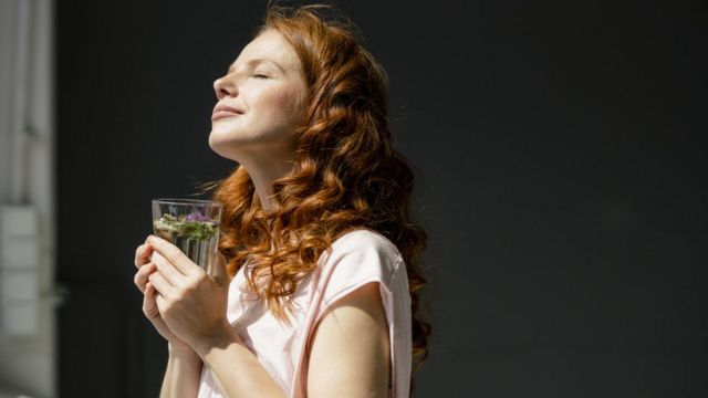 Una mujer respira con un vaso de agua en la mano.