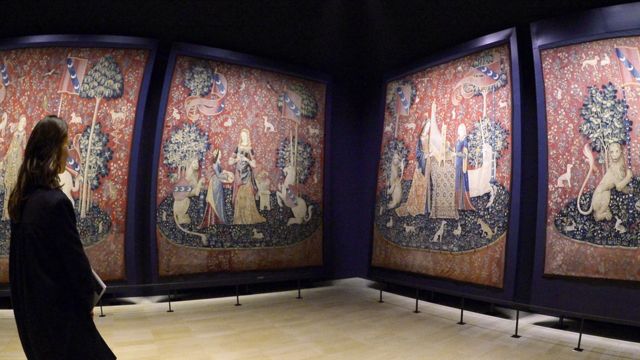 Mulher vendo peças da série de tapeçaria 'A dama e o unicórnio' expostas em galeria