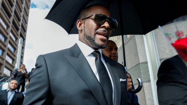 R. Kelly caminhando na rua, seguido por seguranças