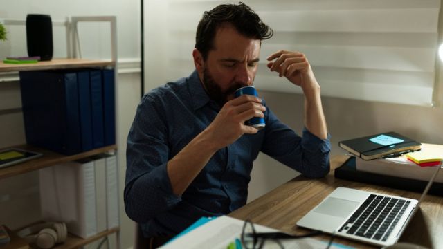 Un hombre toma una bebida energizante para mantenerse despierto en su trabajo