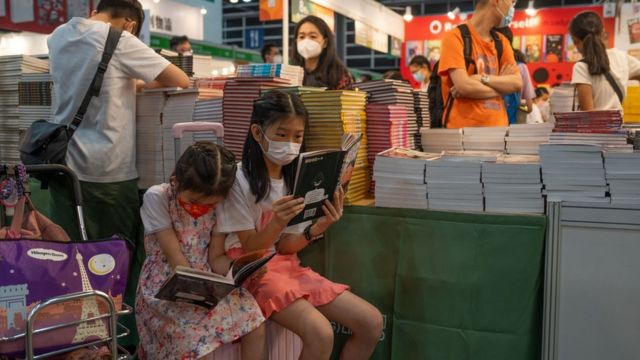 香港书展展场内一对小姊妹在一书摊前坐在行李箱上读书（20/7/2022）